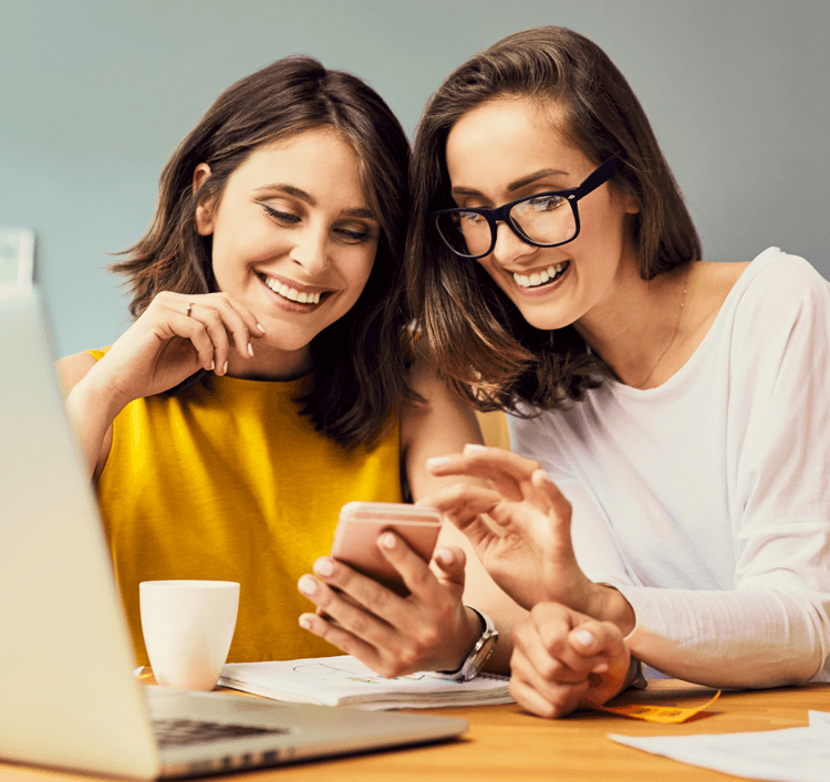 Duas mulheres olhando para o celular e sorrindo